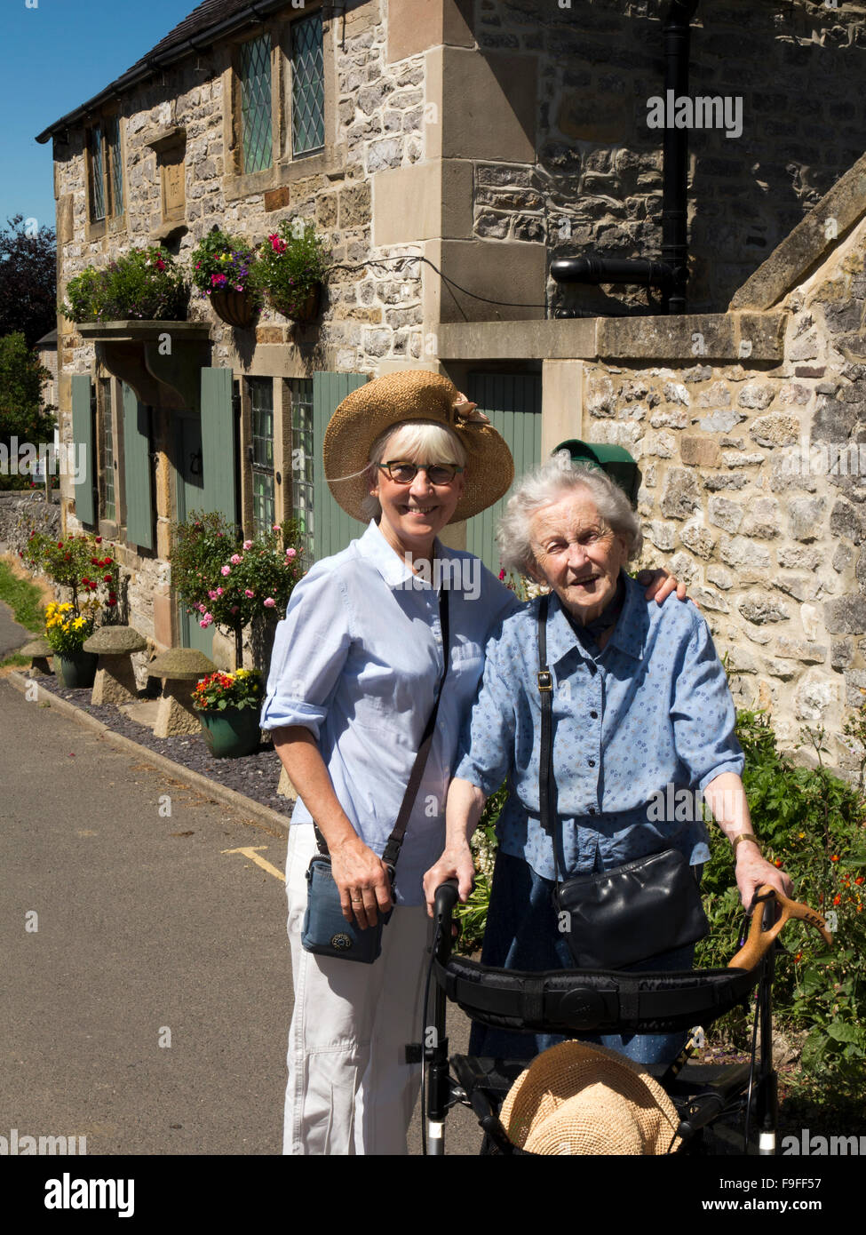 Royaume-uni, Angleterre, Derbyshire, Hartington, Rue de l'Église, mère âgée à l'aide de walker avec de hauts fille Banque D'Images