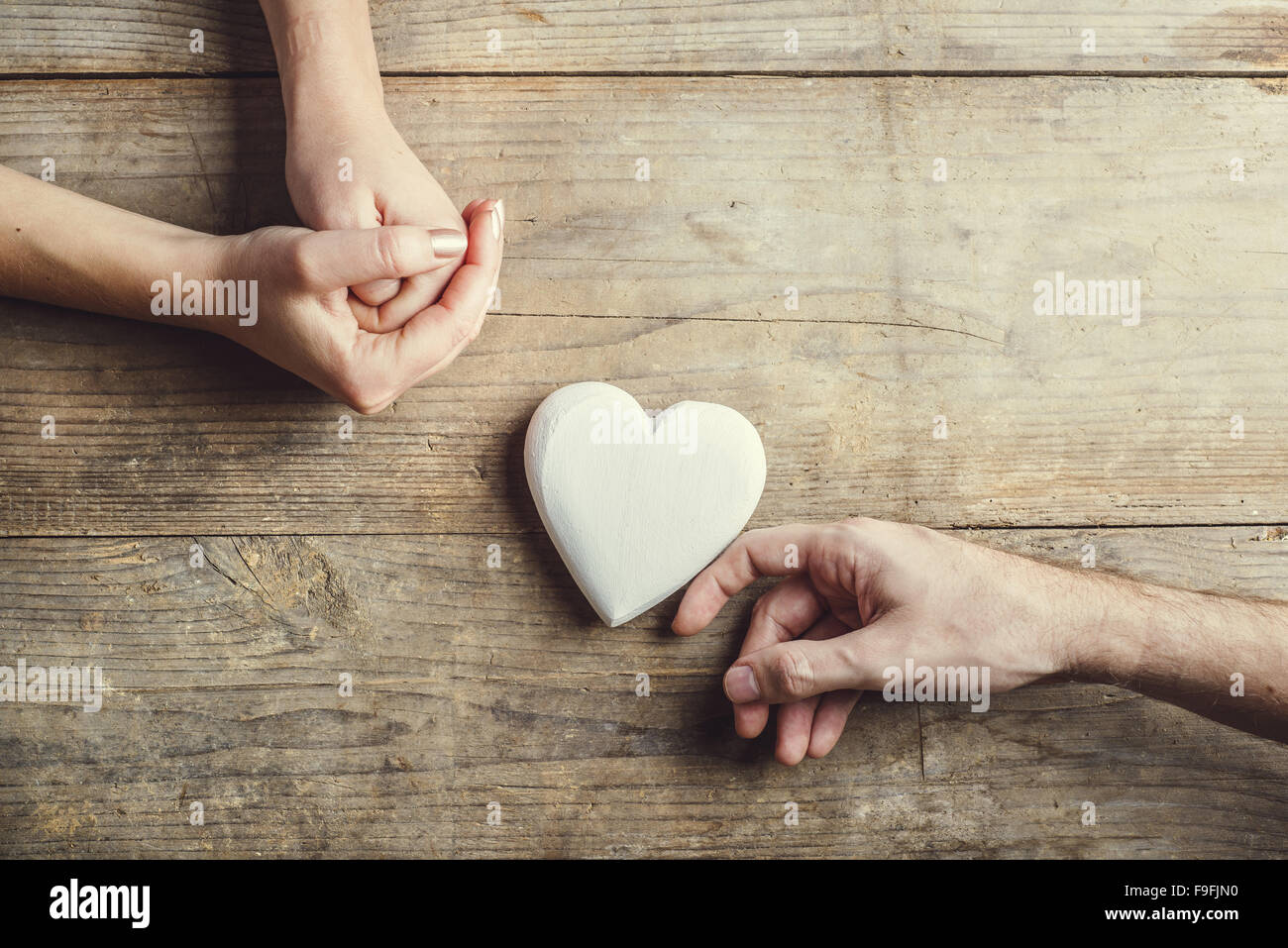 Offrant un homme tendrement coeur blanc à une femme. Studio shot sur un fond de bois, vue de dessus. Banque D'Images