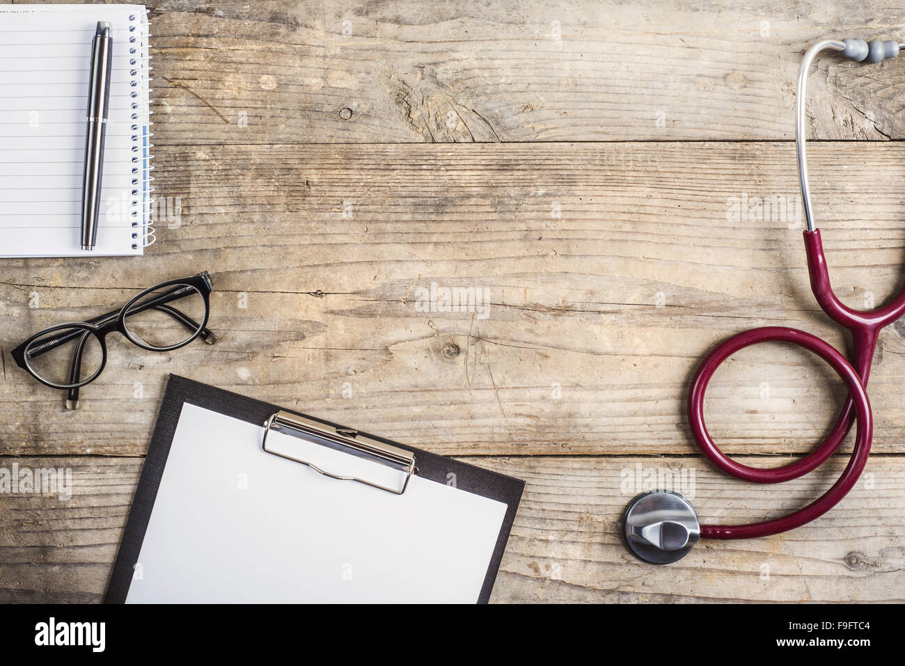 Poste de travail d'un médecin. Stéthoscope, papiers, verres et autres choses sur fond d'un bureau en bois. Banque D'Images