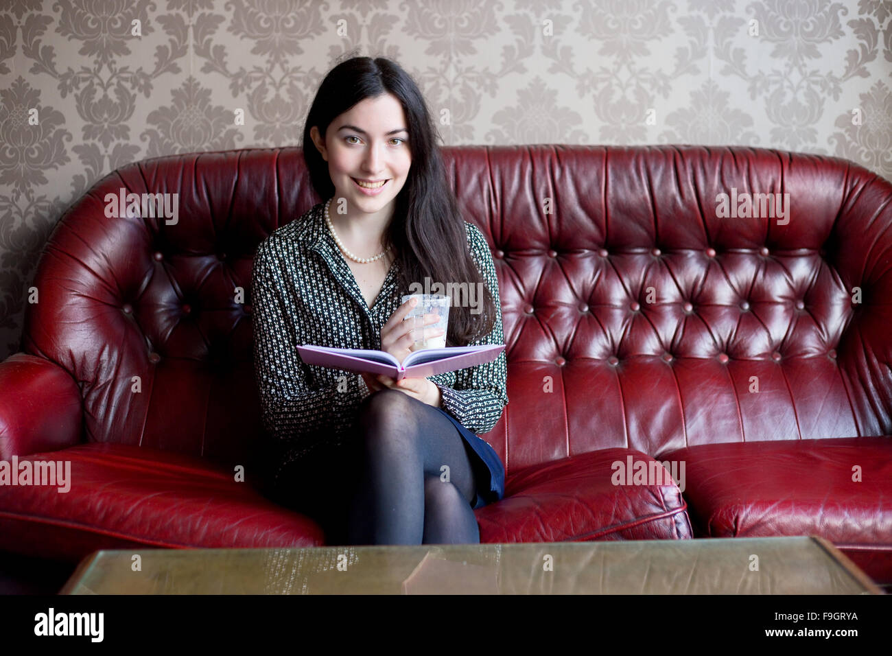 Jeune femme assise sur un canapé avec un livre et un verre Photo Stock -  Alamy