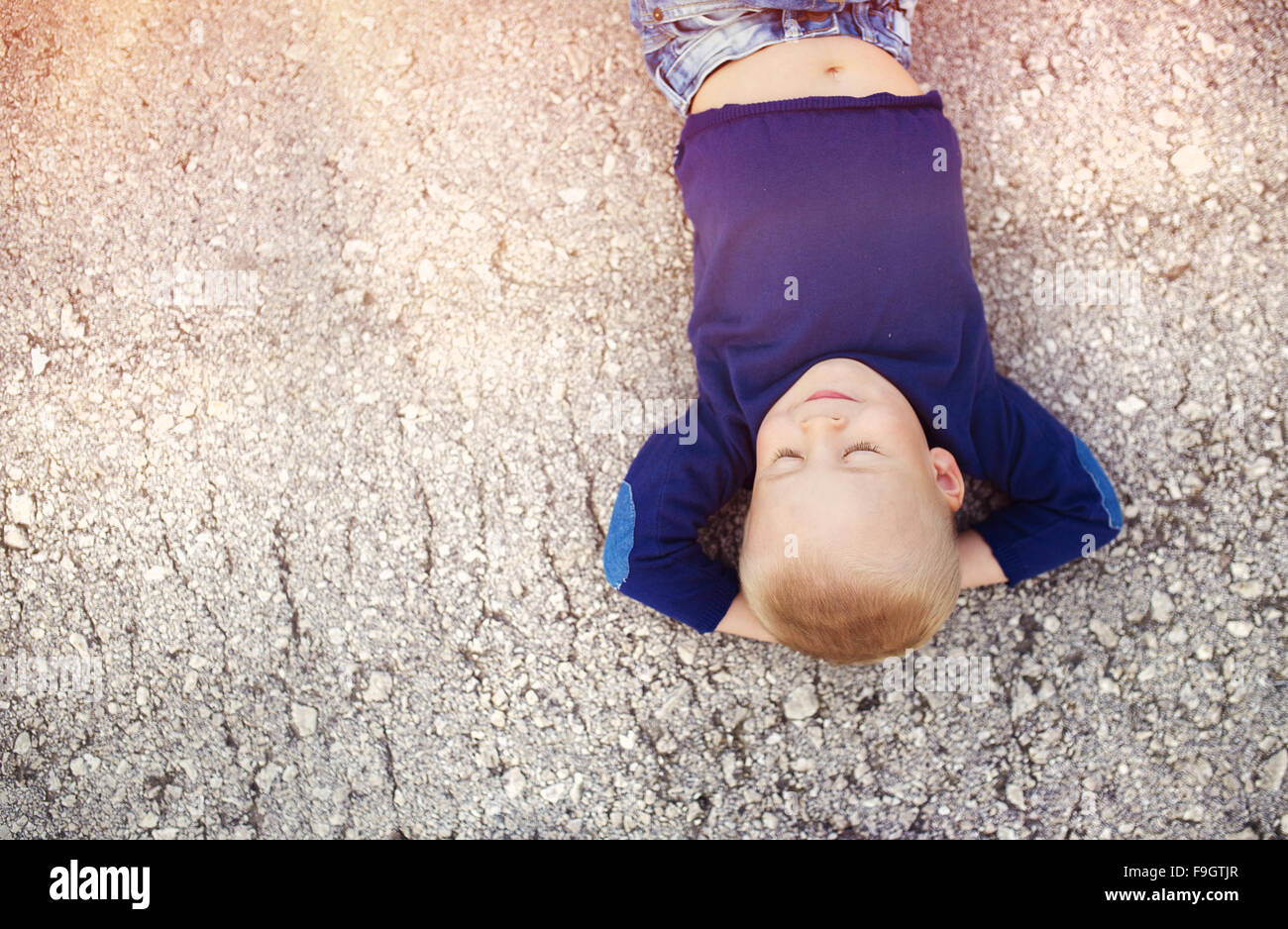 Petit garçon allongé sur le sol en son temps à l'extérieur Banque D'Images