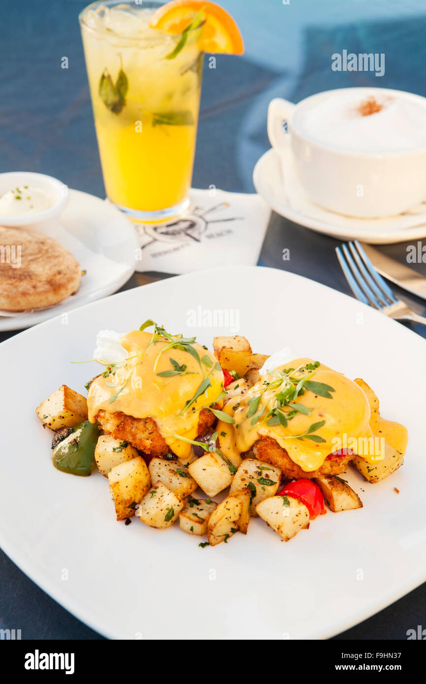 Œufs pochés sur des beignets de crabe dormeur sur un lit de pommes de terre et petit-déjeuner garni de sauce hollandaise chipotle, avocat et pico de Banque D'Images