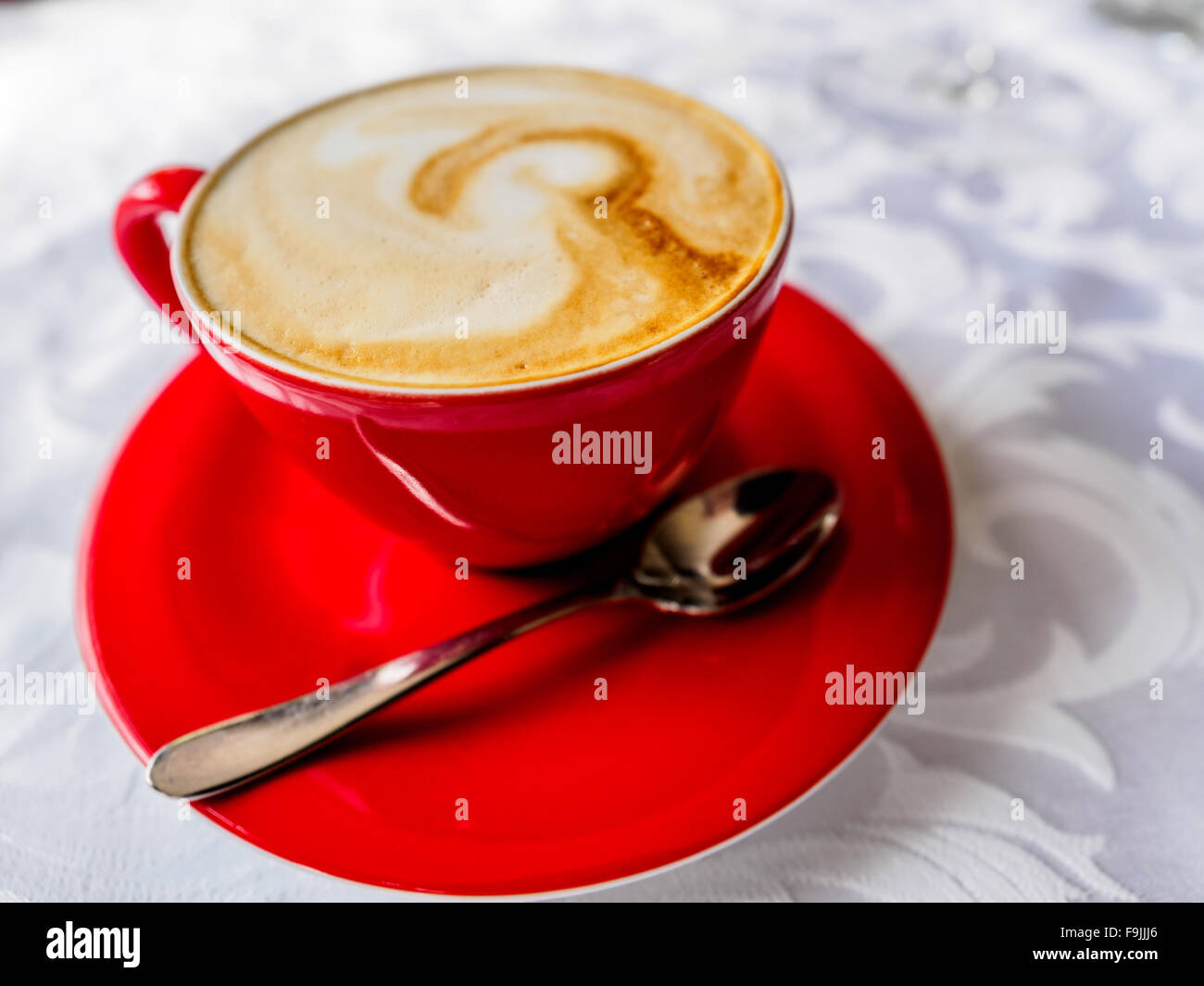 Tasse de cappuccino rouge sur une assiette avec une cuillère à café Banque D'Images