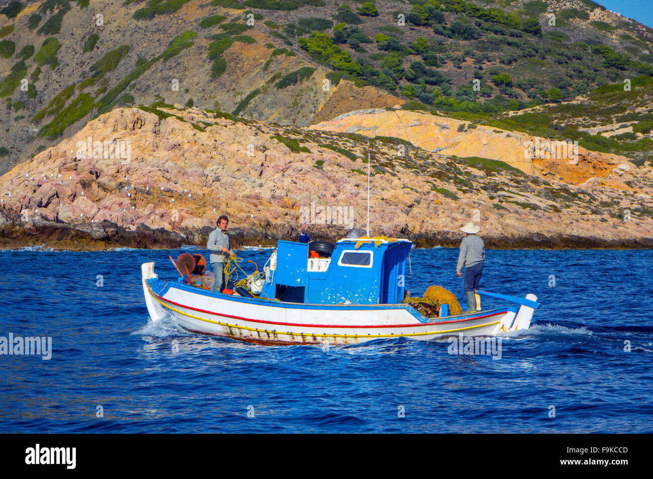 Blanc et bleu petit bateau de pêche, avec deux pêcheurs, mer bleue et de la côte rocheuse Banque D'Images