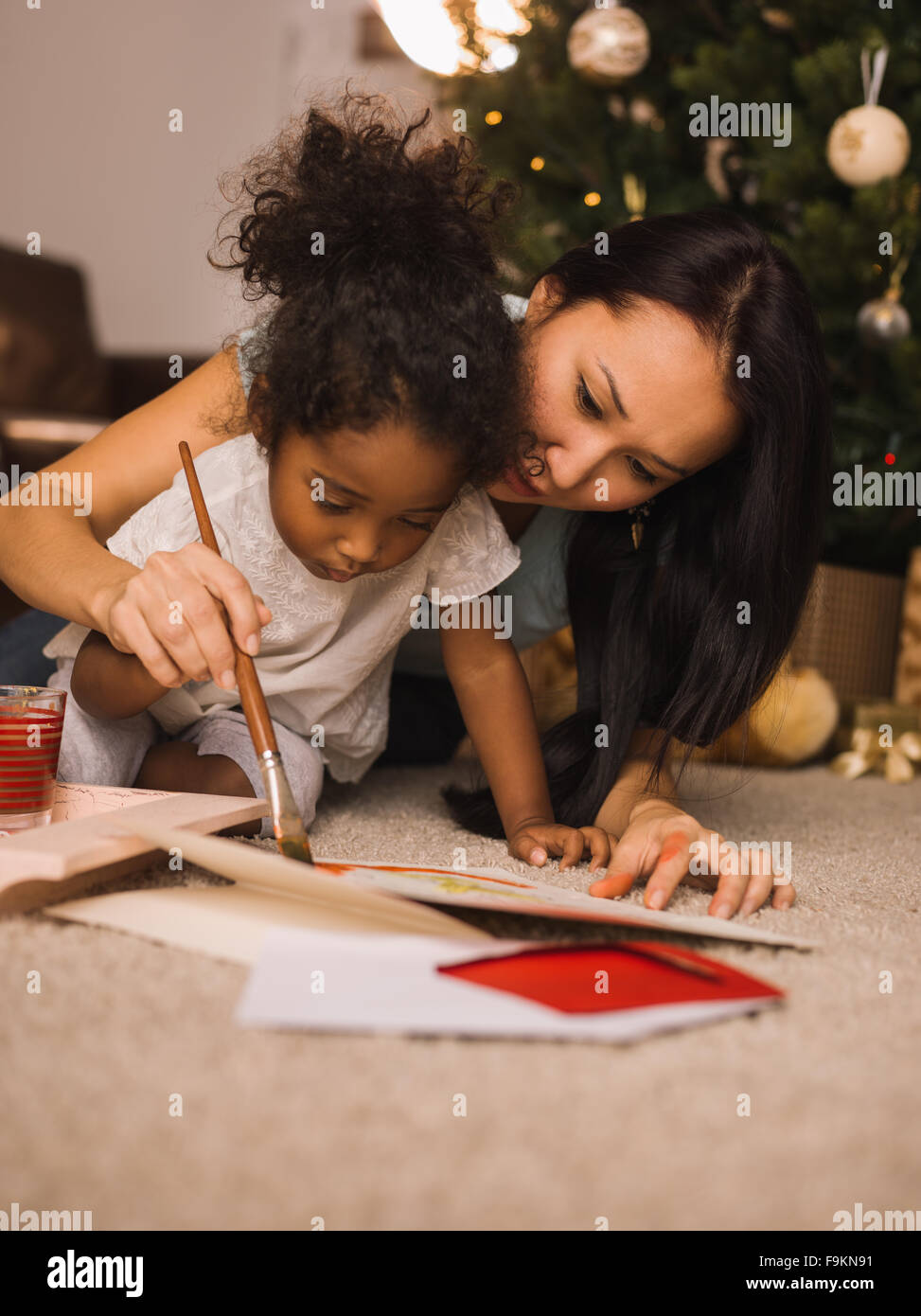 Mixed Race mère et fille jouer et peinture près de l'arbre de Noël à la maison Banque D'Images