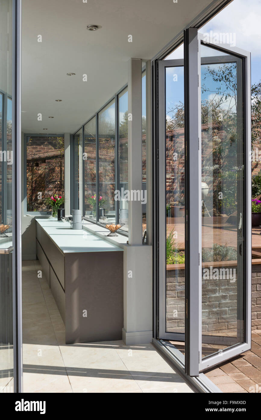 Arrière de la maison, et bi-fold de l'ouverture des portes de la Cuisine sur terrasse. Des murs de verre. Une maison familiale moderne. Banque D'Images