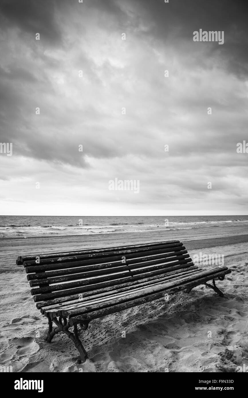 Vieux banc en bois vide sur une plage de sable fin, la côte de la mer Méditerranée. Photo en noir et blanc Banque D'Images