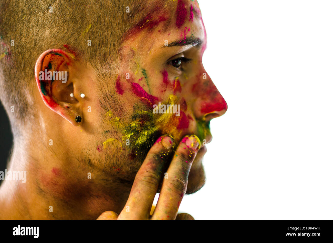 Vue de côté de l'homme visage peint avec l'application de poudres de couleurs de Holi. Isolé sur fond blanc. Close-up. Banque D'Images