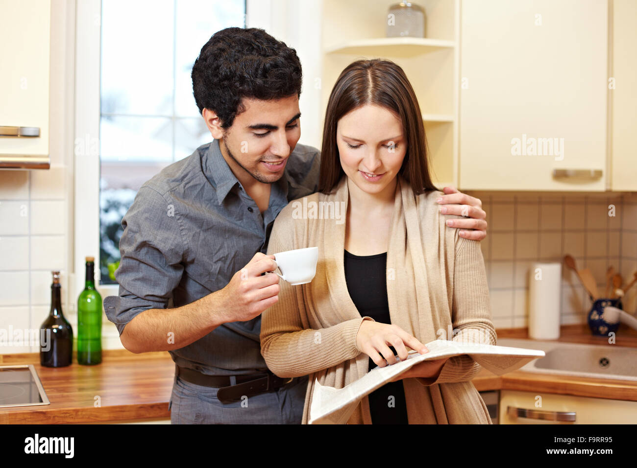 Jeune couple lisant un journal ensemble dans la cuisine Banque D'Images