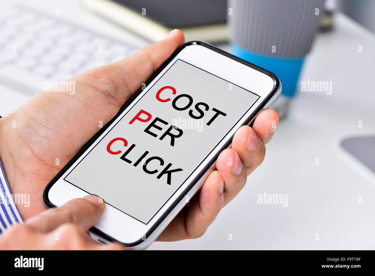 Libre d'un homme assis à son bureau avec un smartphone dans ses mains avec le coût par clic texte écrit dans son s Banque D'Images