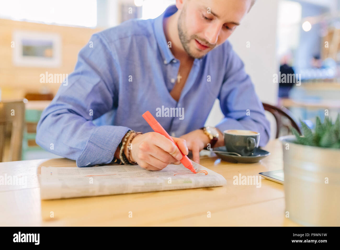 Homme assis dans un café marquant quelque chose dans un journal Banque D'Images