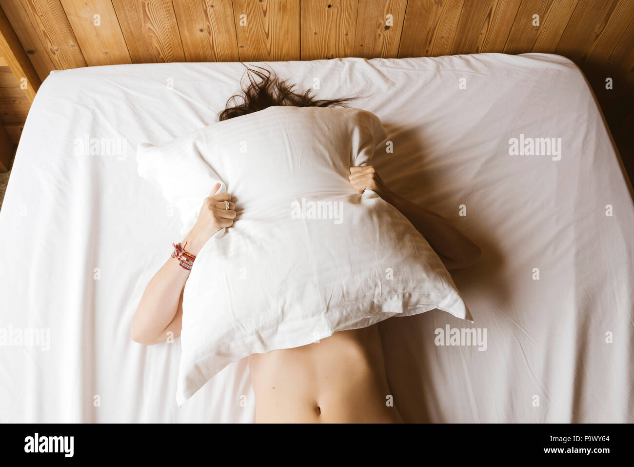 Woman lying on bed couvrant son visage avec un oreiller Banque D'Images