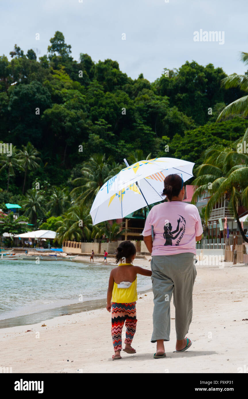 Mère et fille marchant sur la plage de sable blanc avec parapluie Banque D'Images