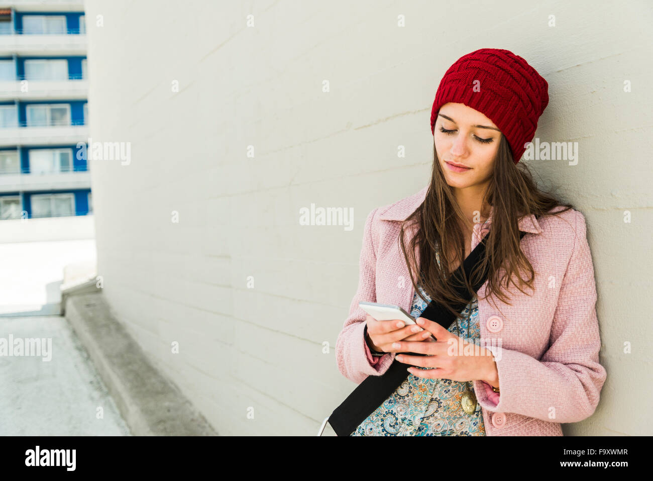 Jeune femme appuyée contre un mur de béton looking at cell phone Banque D'Images