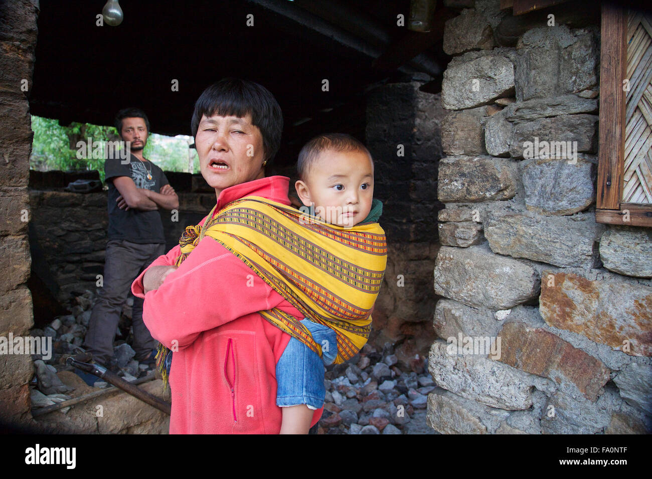 Une femme avec son jeune enfant exécutant une pierre chaude baignoire installation pour les touristes de sa maison à Paro, Bhoutan. Banque D'Images
