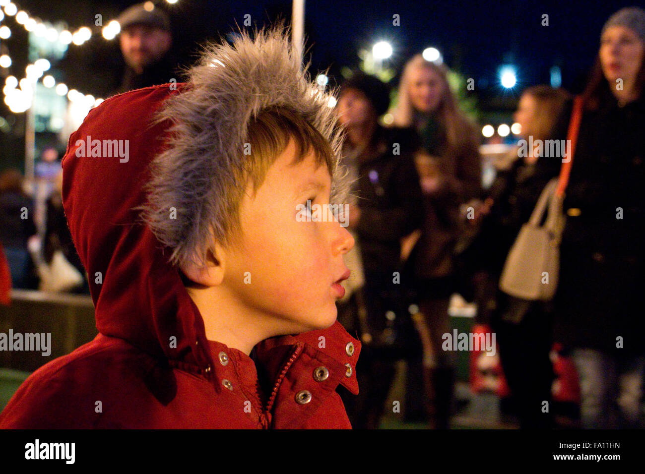 Jeune garçon dans un manteau rouge dans une foule de gens au marché de Noël d'Édimbourg. Banque D'Images