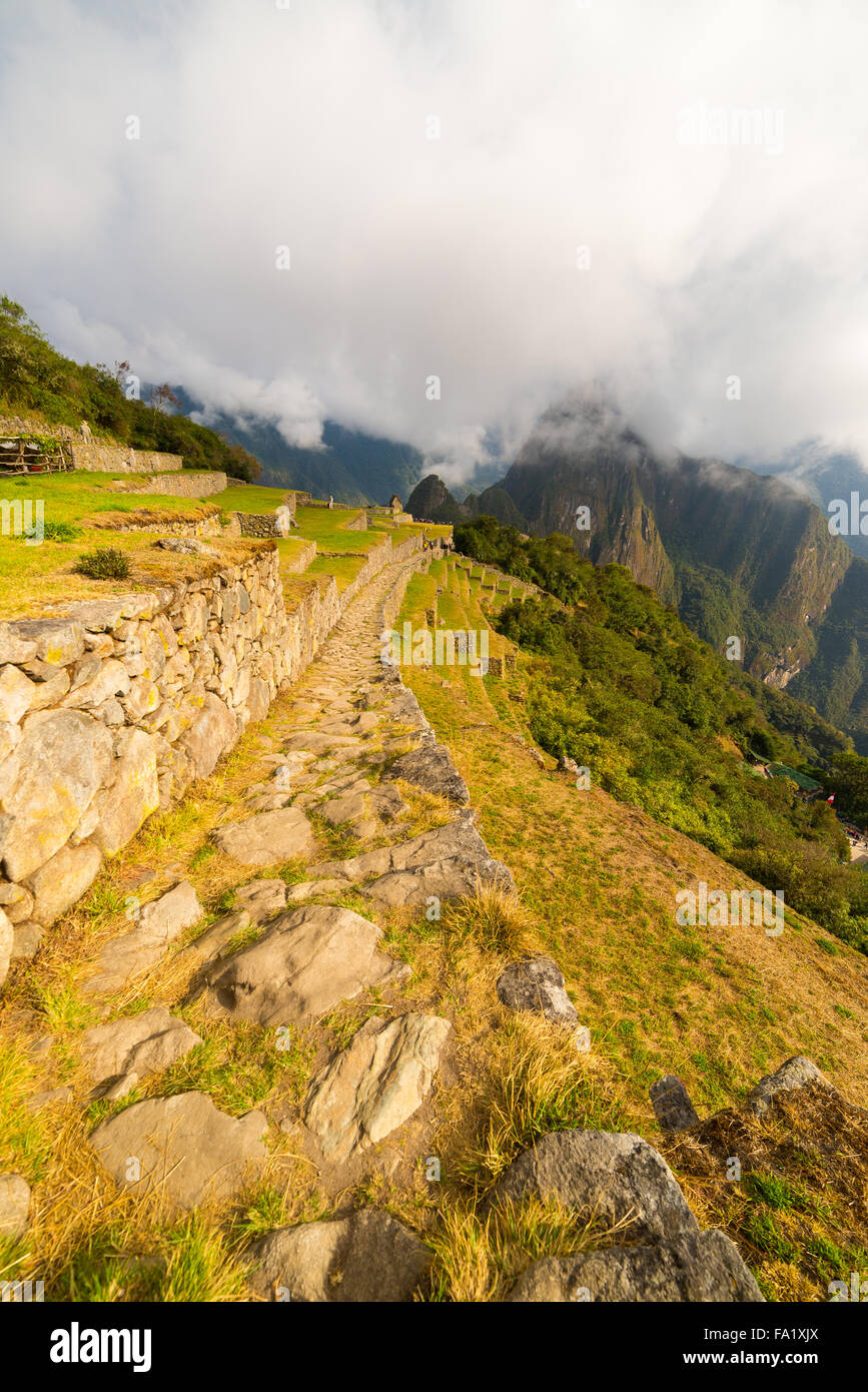 Maison mitoyenne à Machu Picchu chemin illuminé par les premiers rayons du soleil qui sort de l'ouverture des nuages. La ville de l'Inca est le plus Banque D'Images