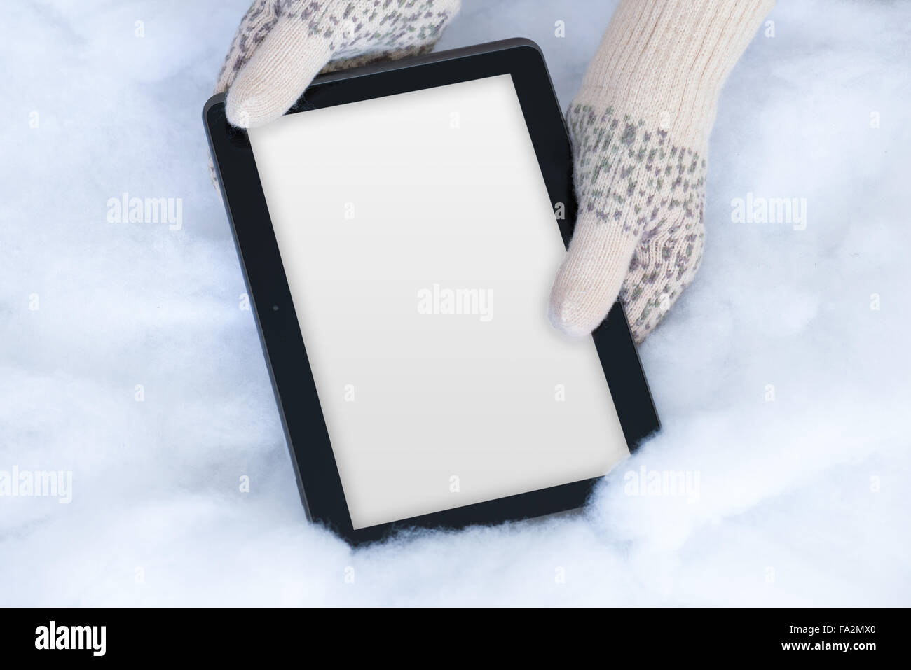 À la lumière des mains femme mitaines tricotés sarcelles sont modernes holding tablet pc avec écran blanc sur fond de neige. Concept d'hiver. Banque D'Images