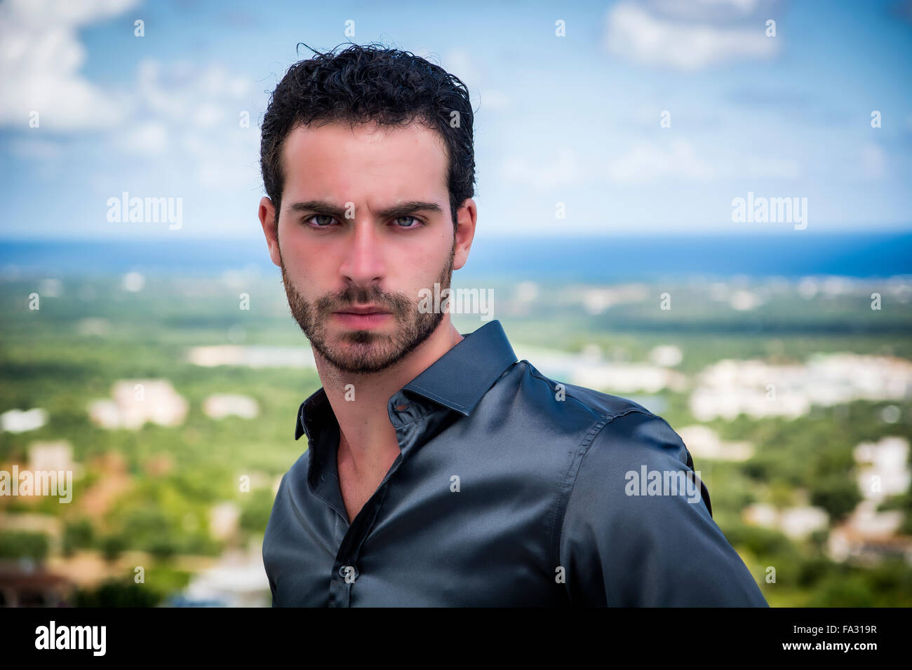Portrait de jeune homme séduisant élégant avec des cheveux bouclés debout contre de rives et à la recherche d'un côté avec sérieux Banque D'Images