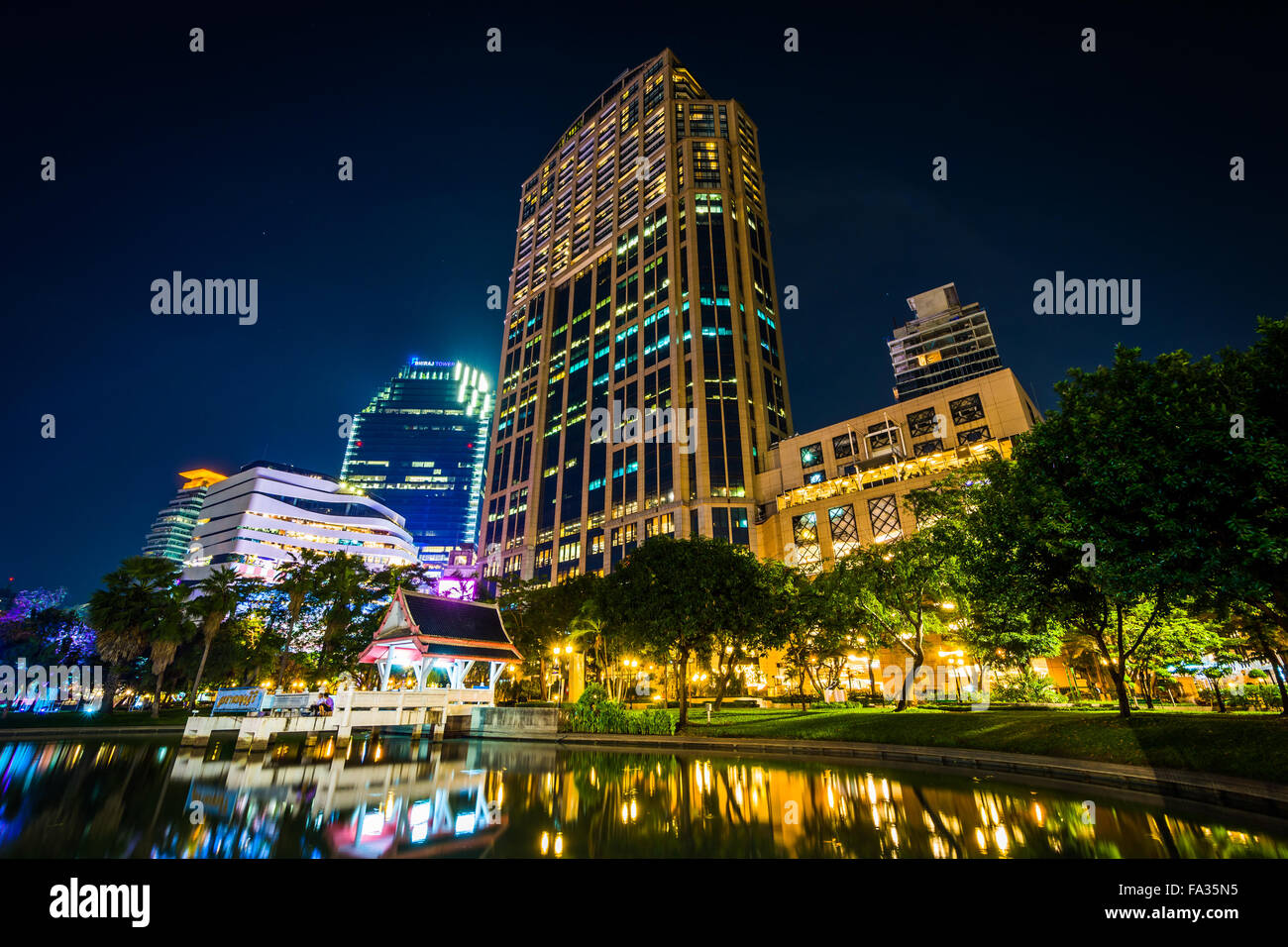Les gratte-ciel modernes et du lac la nuit, vu au parc Benjasiri, à Bangkok, Thaïlande. Banque D'Images