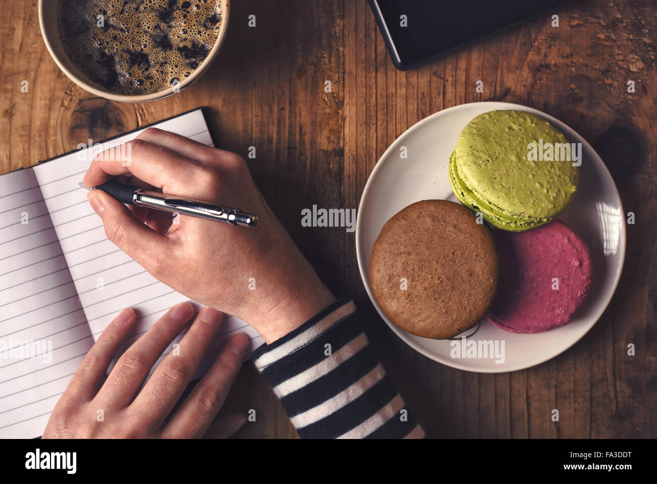 Businessman au petit-déjeuner, vue du dessus de la main avec un crayon, tasse de café, un téléphone mobile et macaron cookie Banque D'Images