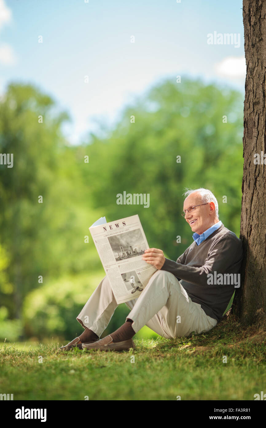 Shot verticale d'un senior joyeux gentleman lire un journal assis sur le gazon dans un parc Banque D'Images