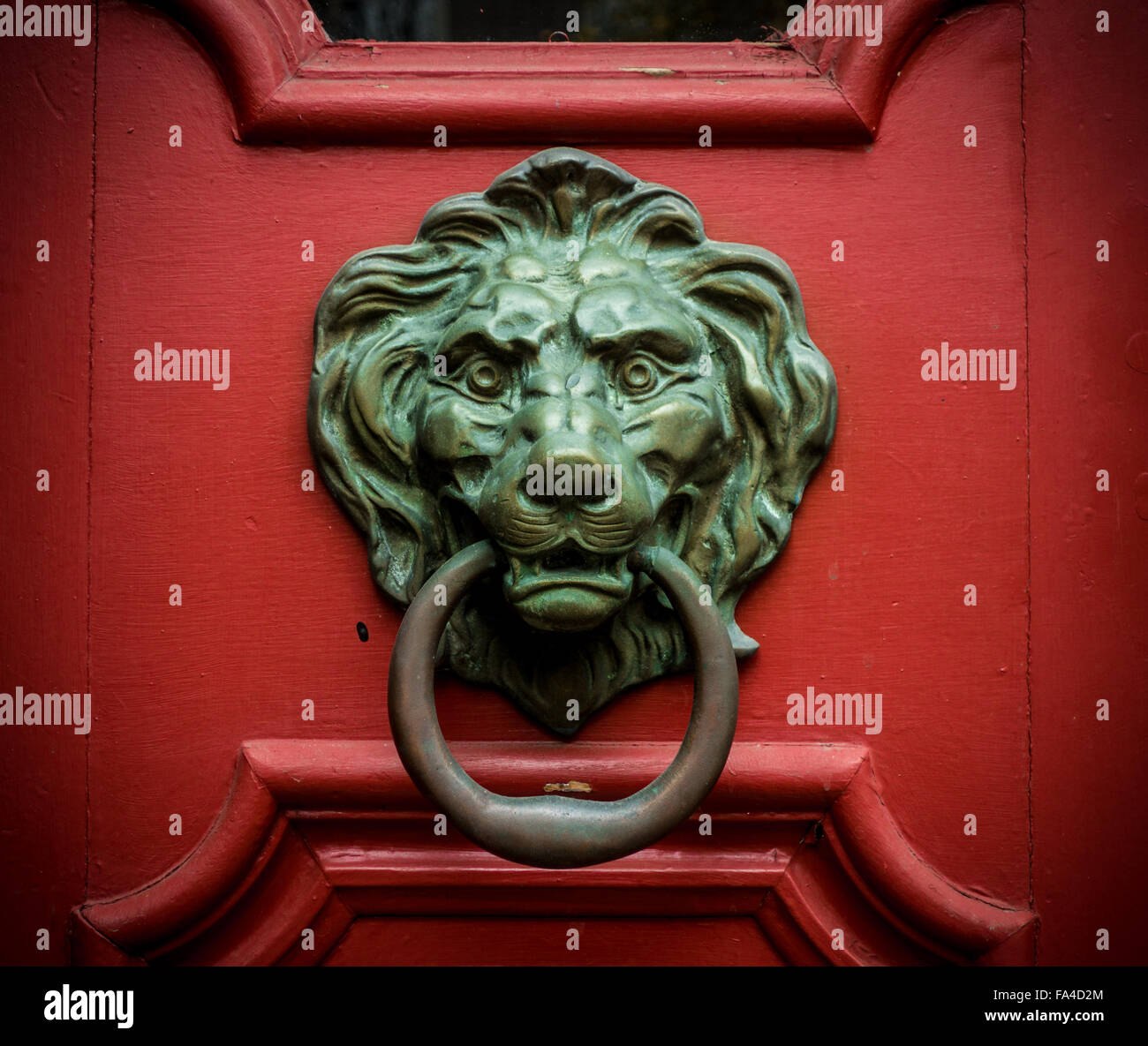 Une tête de lion avec un anneau dans sa bouche est un doorknocker sur une porte en bois rouge. Banque D'Images