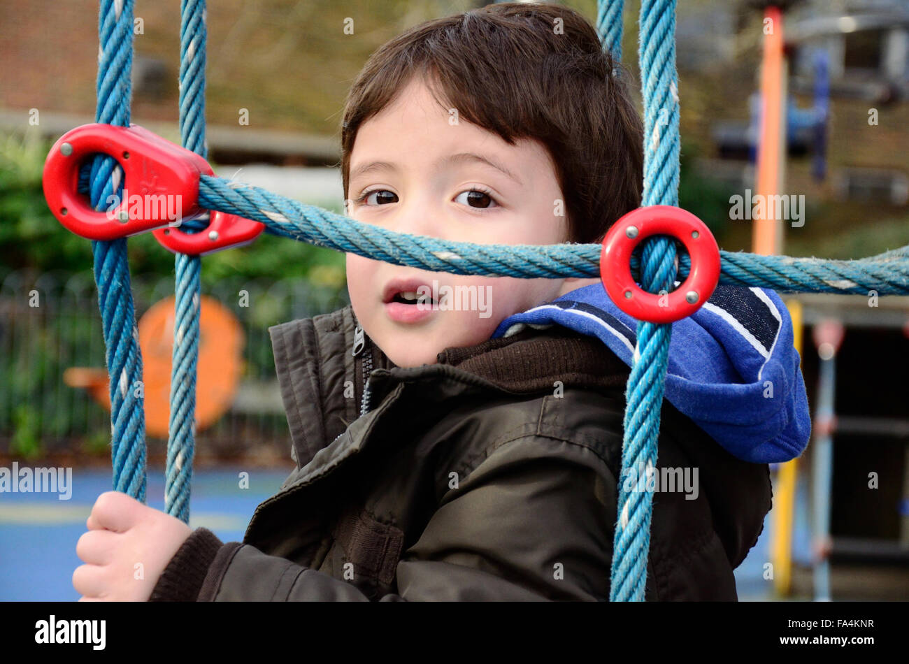 Un jeune garçon jouant sur un filet qui fait partie d'une escalade dans une aire de jeux pour enfants. Banque D'Images