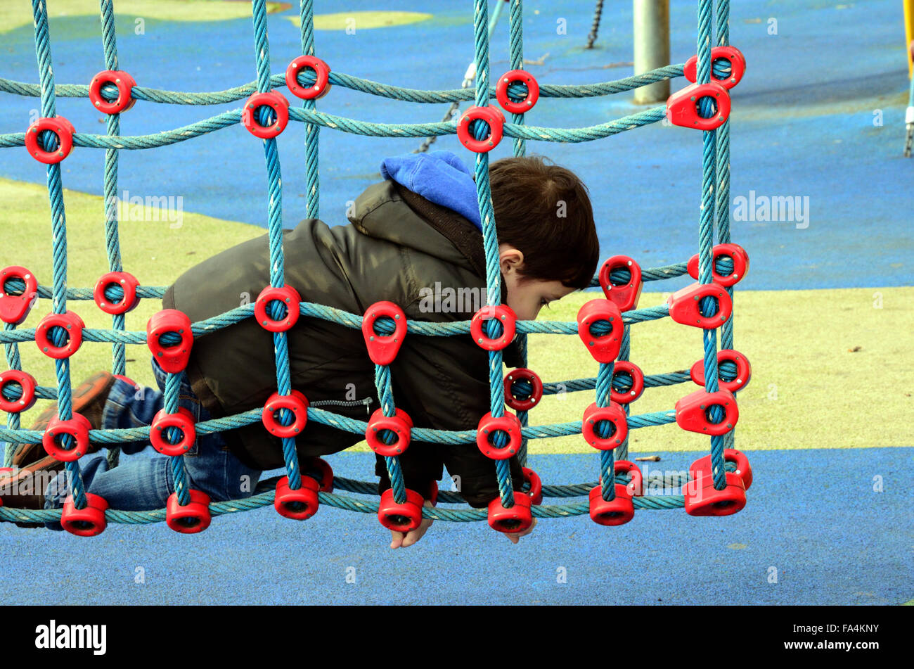 Un jeune garçon jouant sur un filet qui fait partie d'une escalade dans une aire de jeux pour enfants. Banque D'Images