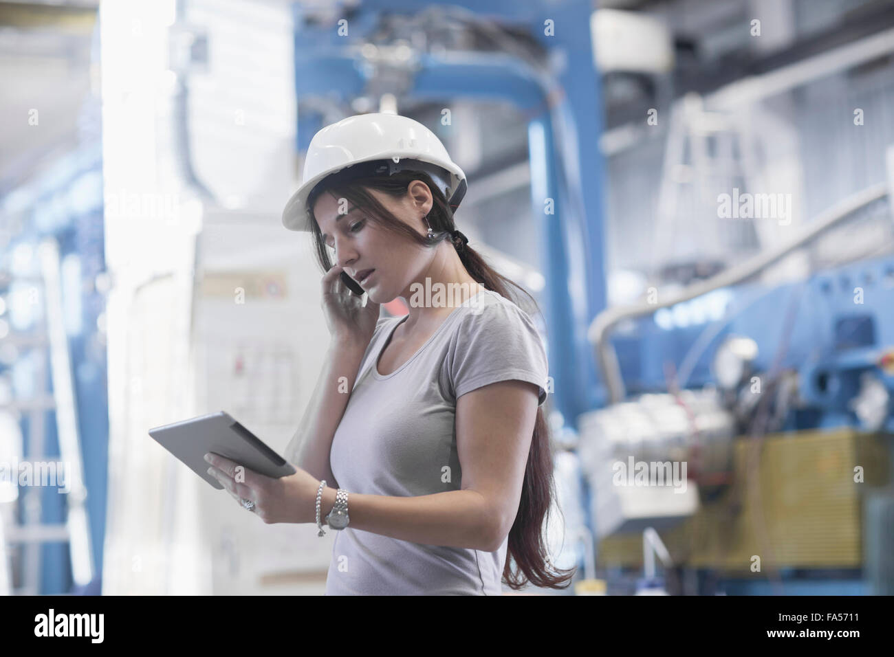 Ingénieur femelle à l'aide d'une tablette numérique et le téléphone mobile dans une installation industrielle, Bade-Wurtemberg, Allemagne Banque D'Images