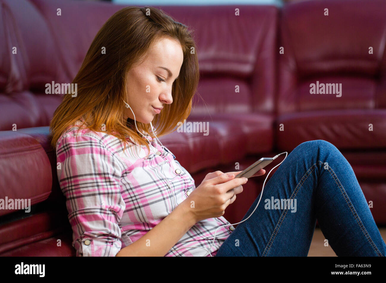 Pensive jolie jeune femme assise près d'un canapé et d'écouter de la musique du smartphone Banque D'Images