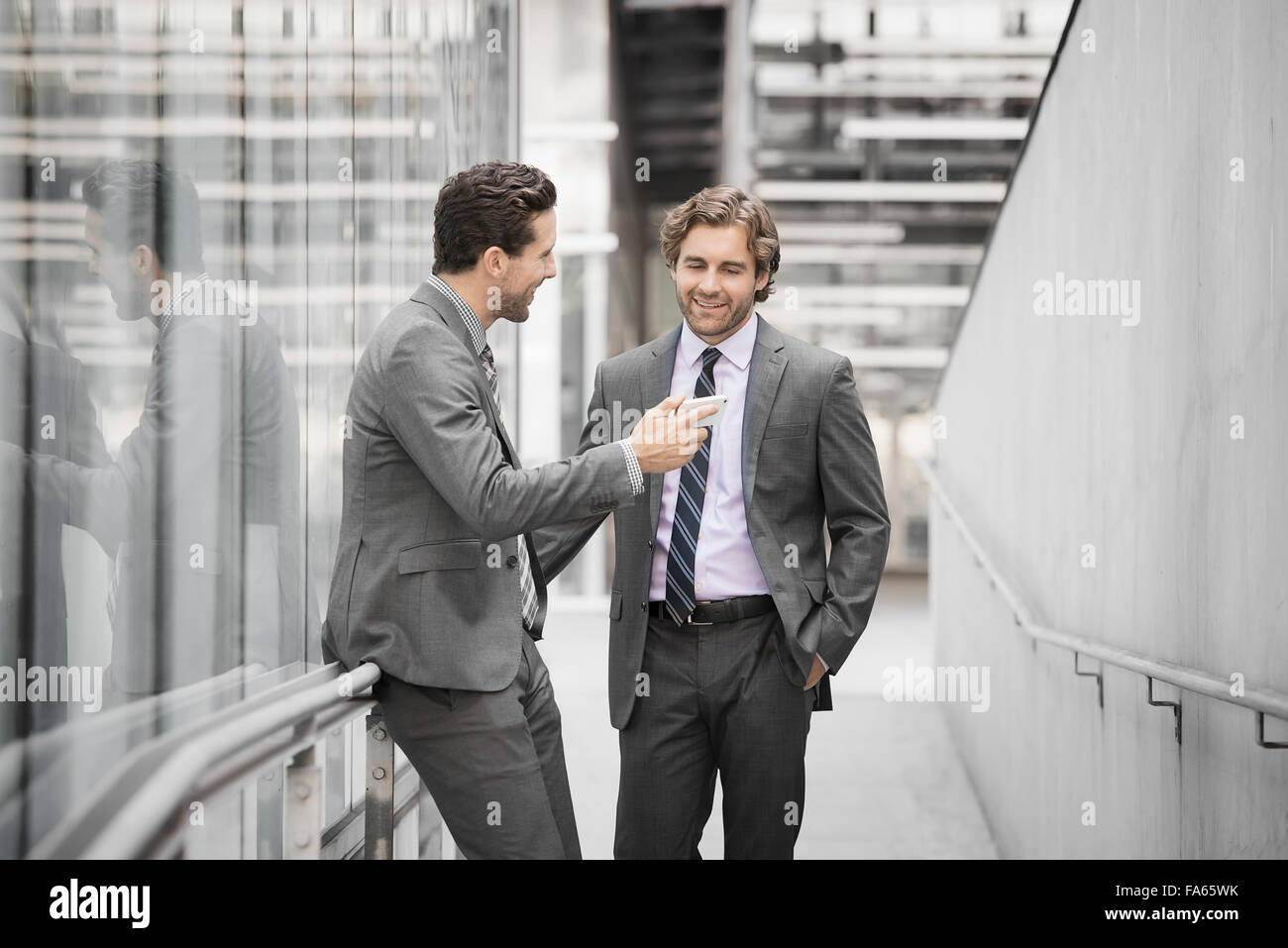 Deux hommes en costumes d'affaires à l'extérieur d'un grand bâtiment, l'un tenant un téléphone intelligent. Banque D'Images