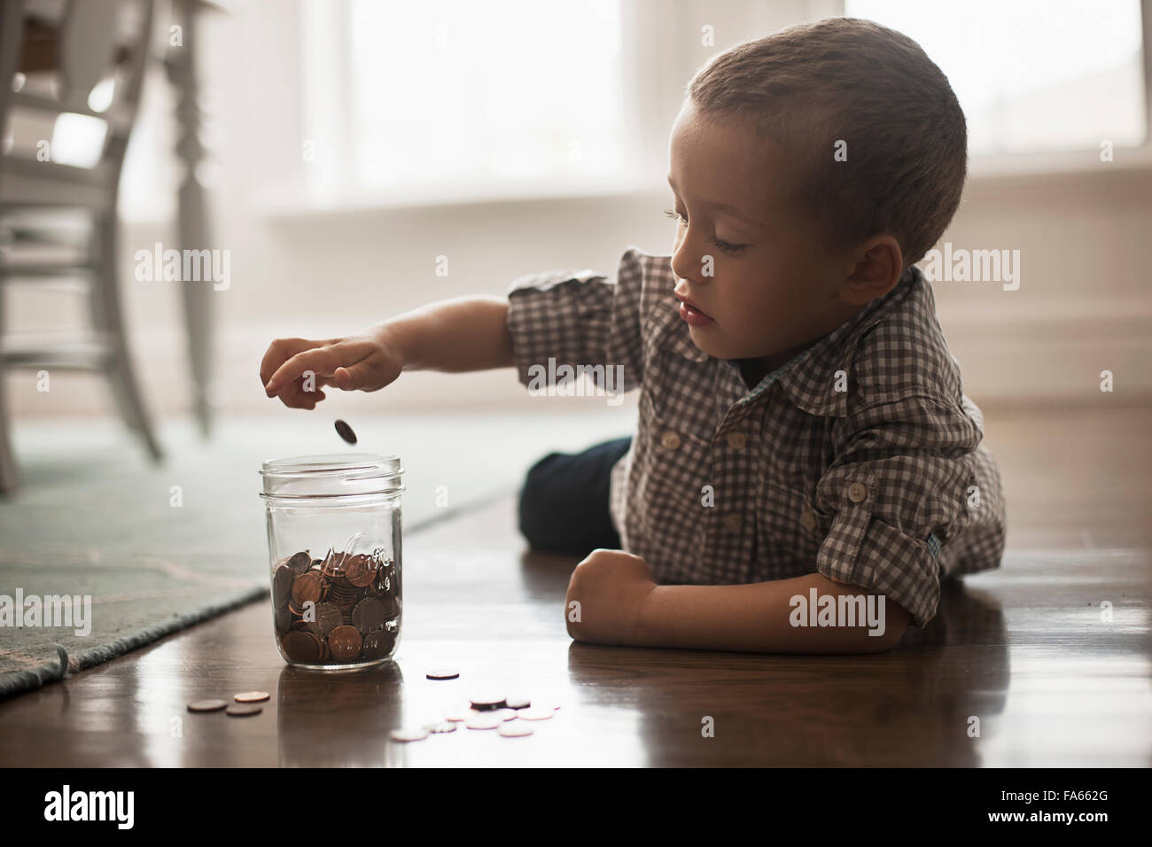 Un enfant couché sur le ventre sur le sol en jouant avec des pièces de monnaie et les mettre dans un bocal de verre. Banque D'Images