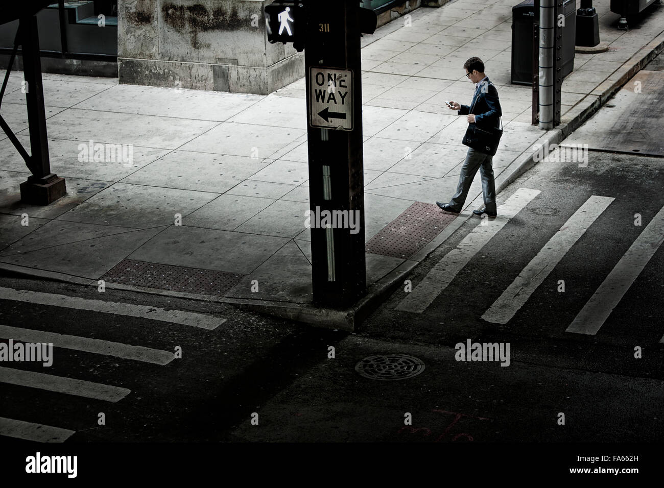 Un homme marchant sur un passage à niveau de la rue, à la recherche d'un téléphone dans sa main. Banque D'Images