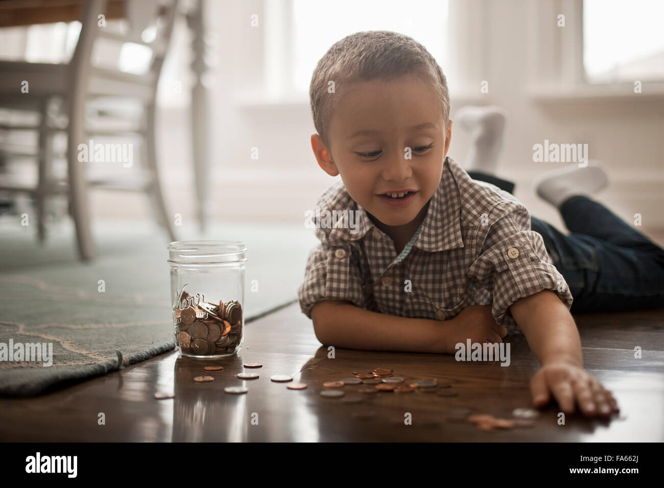Un enfant couché sur le ventre sur le sol en jouant avec des pièces de monnaie et les mettre dans un bocal de verre. Banque D'Images