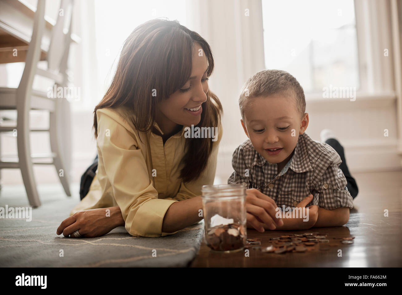 Une femme et un enfant se trouvant sur le plancher, jouant avec le laiton et de pièces d'argent, de les placer dans un bocal en verre. Banque D'Images