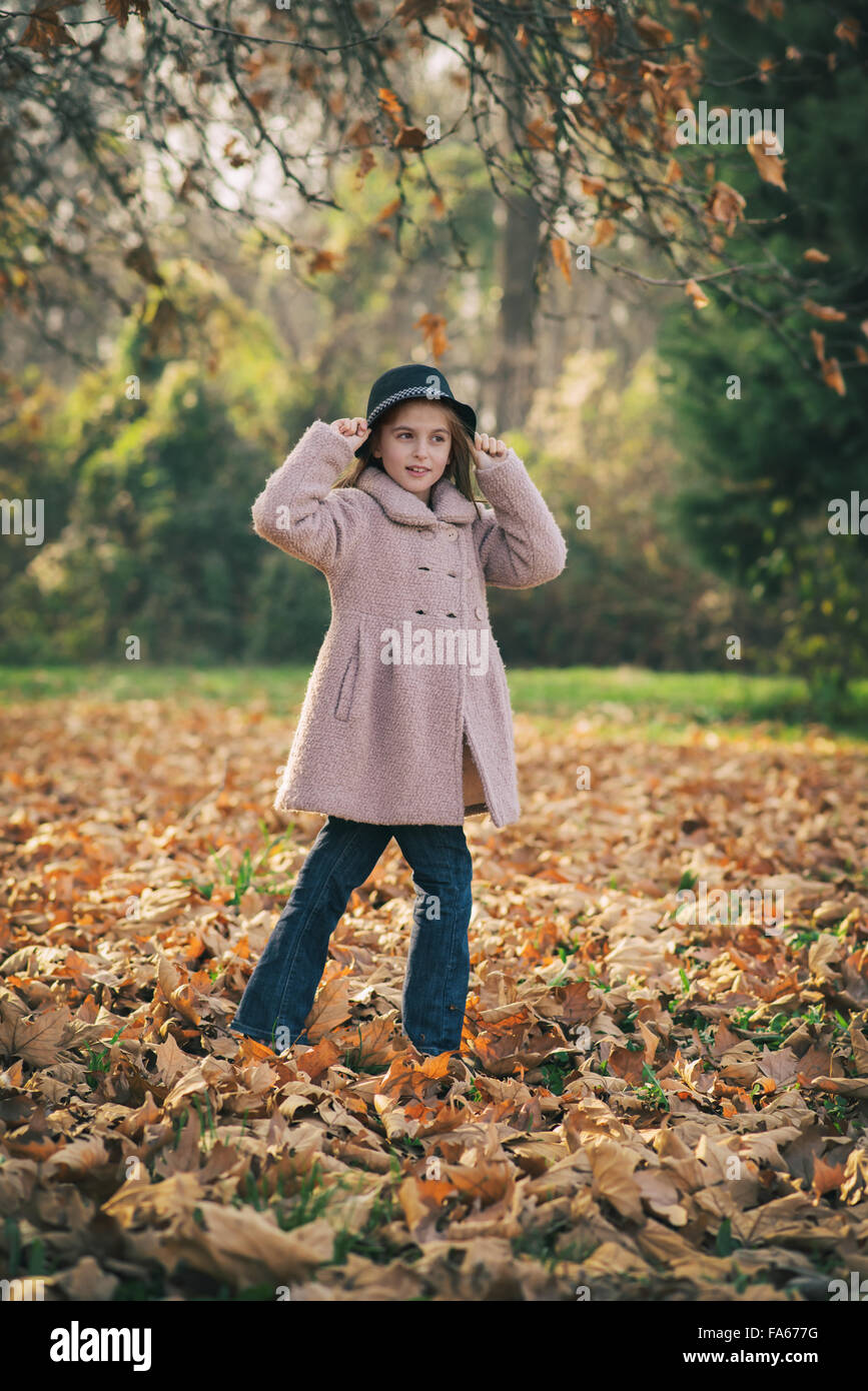 Fille qui marche à travers les feuilles d'automne la maintenant sur son chapeau Banque D'Images
