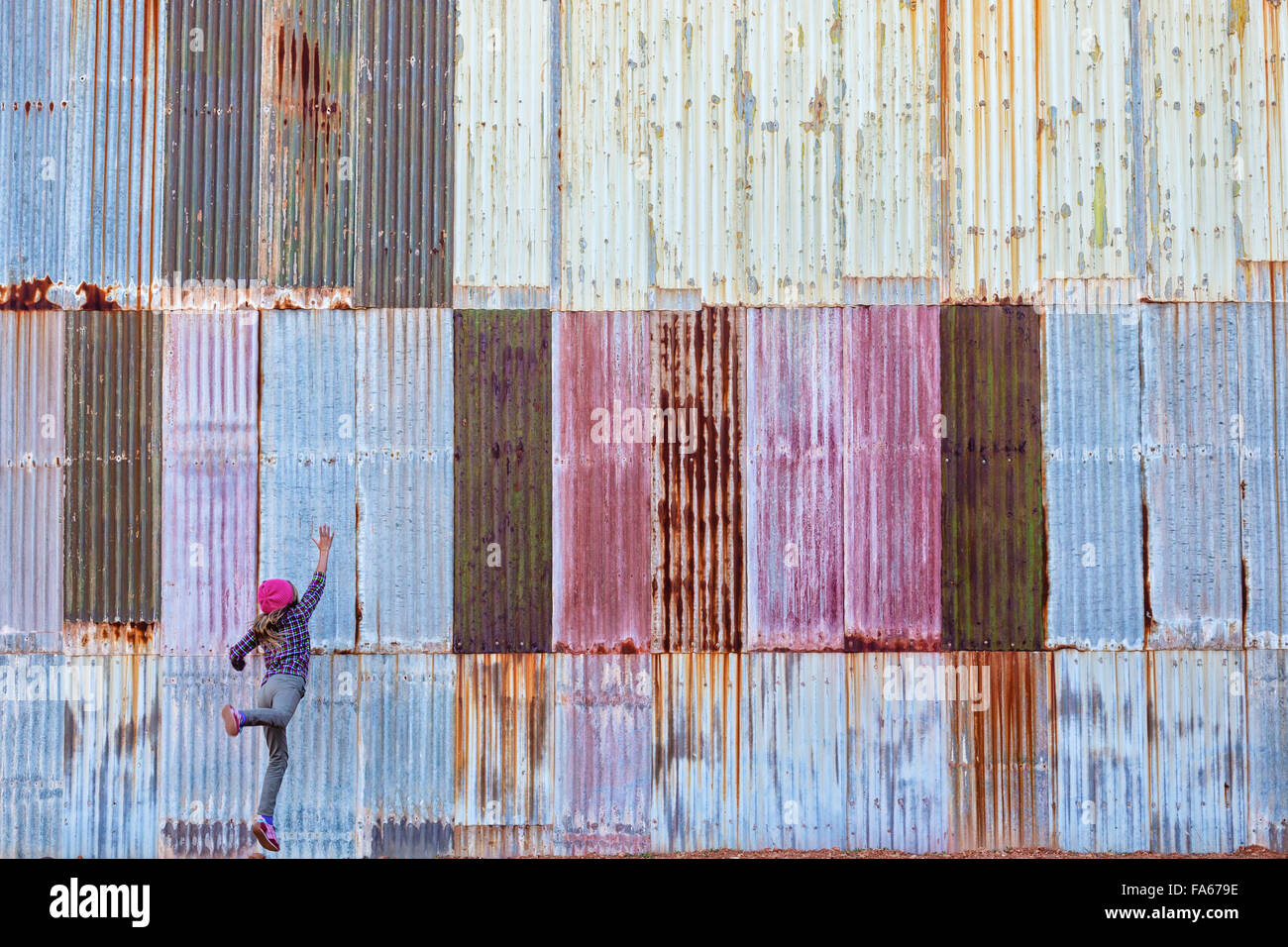 Fille de sauter devant un mur de métal ondulé, Kalgoorlie, Australie occidentale Banque D'Images