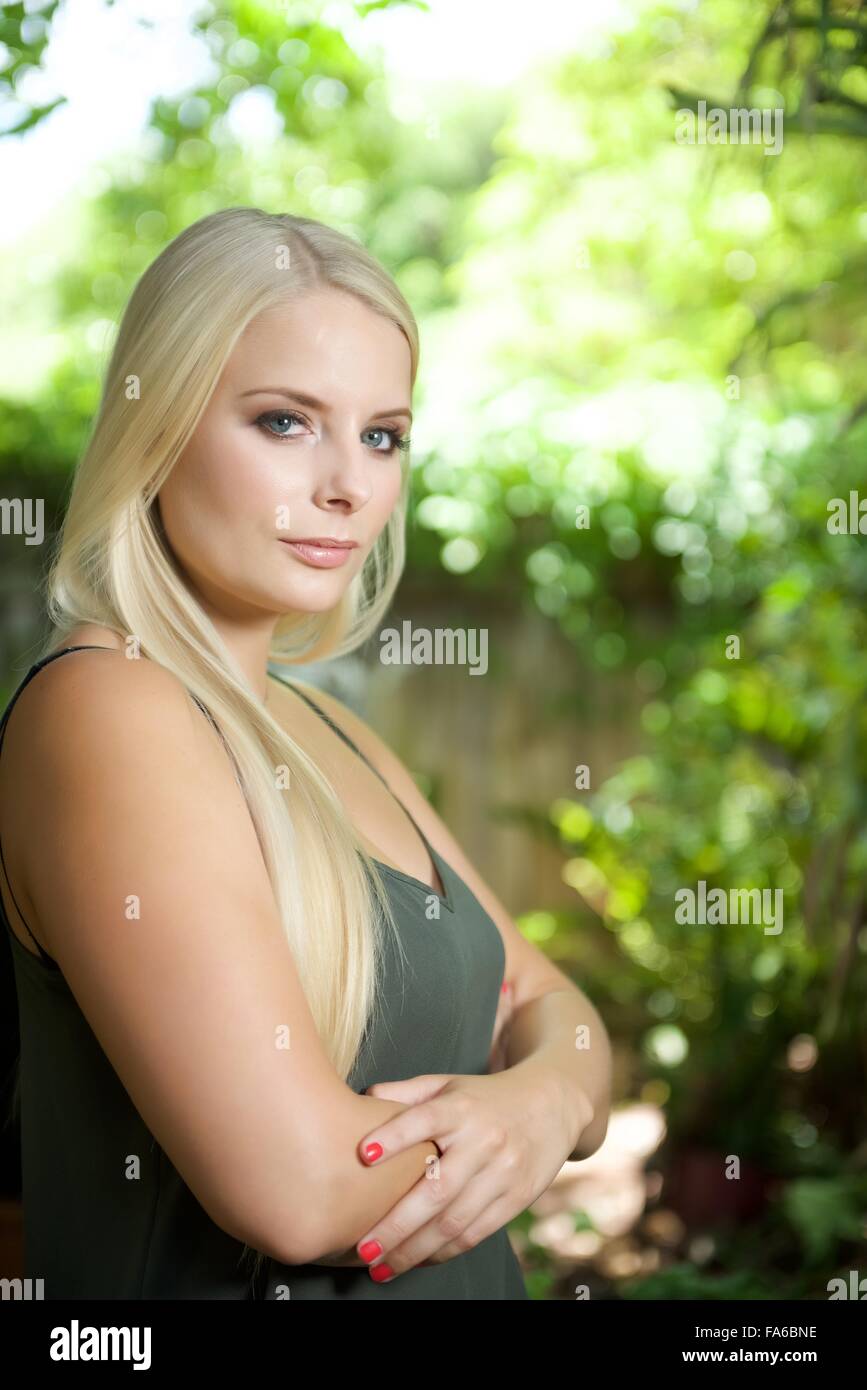Une fille blonde se trouve dans le jardin. Elle porte un top vert olive et à la recherche à l'appareil photo Banque D'Images Une fille blonde se trouve dans le jardin. Elle porte un top vert olive et à la recherche à l'appareil photo Banque D'Images