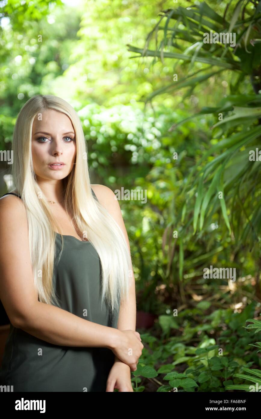 Une fille blonde se trouve dans le jardin. Elle porte un top vert olive et à la recherche à l'appareil photo Banque D'Images Une fille blonde se trouve dans le jardin. Elle porte un top vert olive et à la recherche à l'appareil photo Banque D'Images