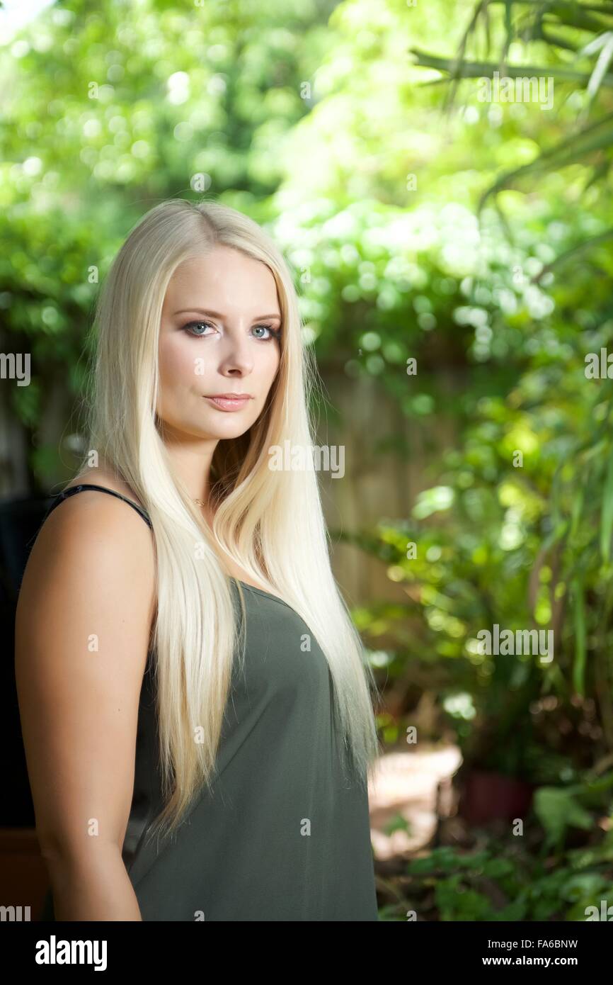 Une fille blonde se trouve dans le jardin. Elle porte un top vert olive et à la recherche à l'appareil photo Banque D'Images Une fille blonde se trouve dans le jardin. Elle porte un top vert olive et à la recherche à l'appareil photo Banque D'Images