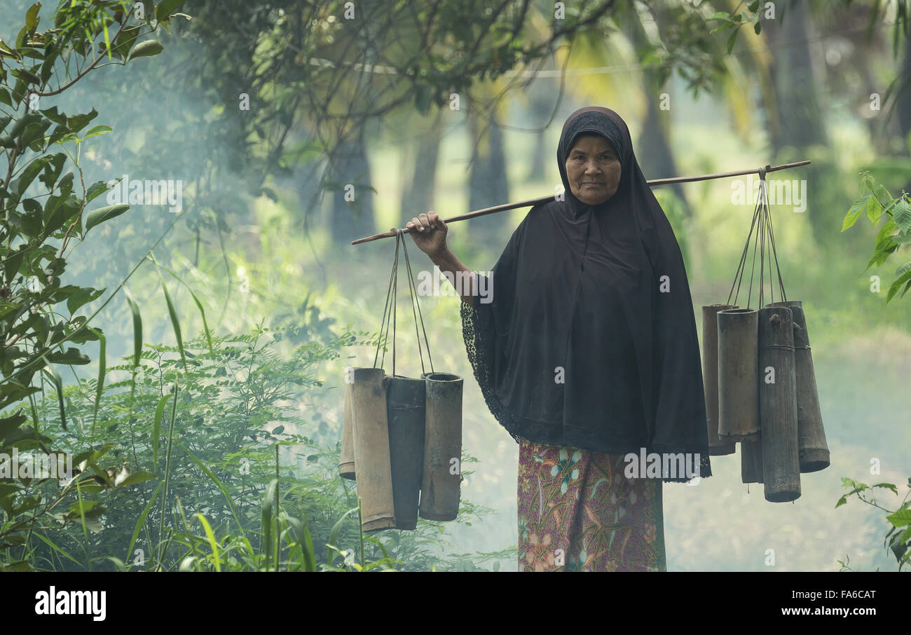 Thai Senior femme transportant des tubes de bambou avec du sucre, Thaïlande Banque D'Images