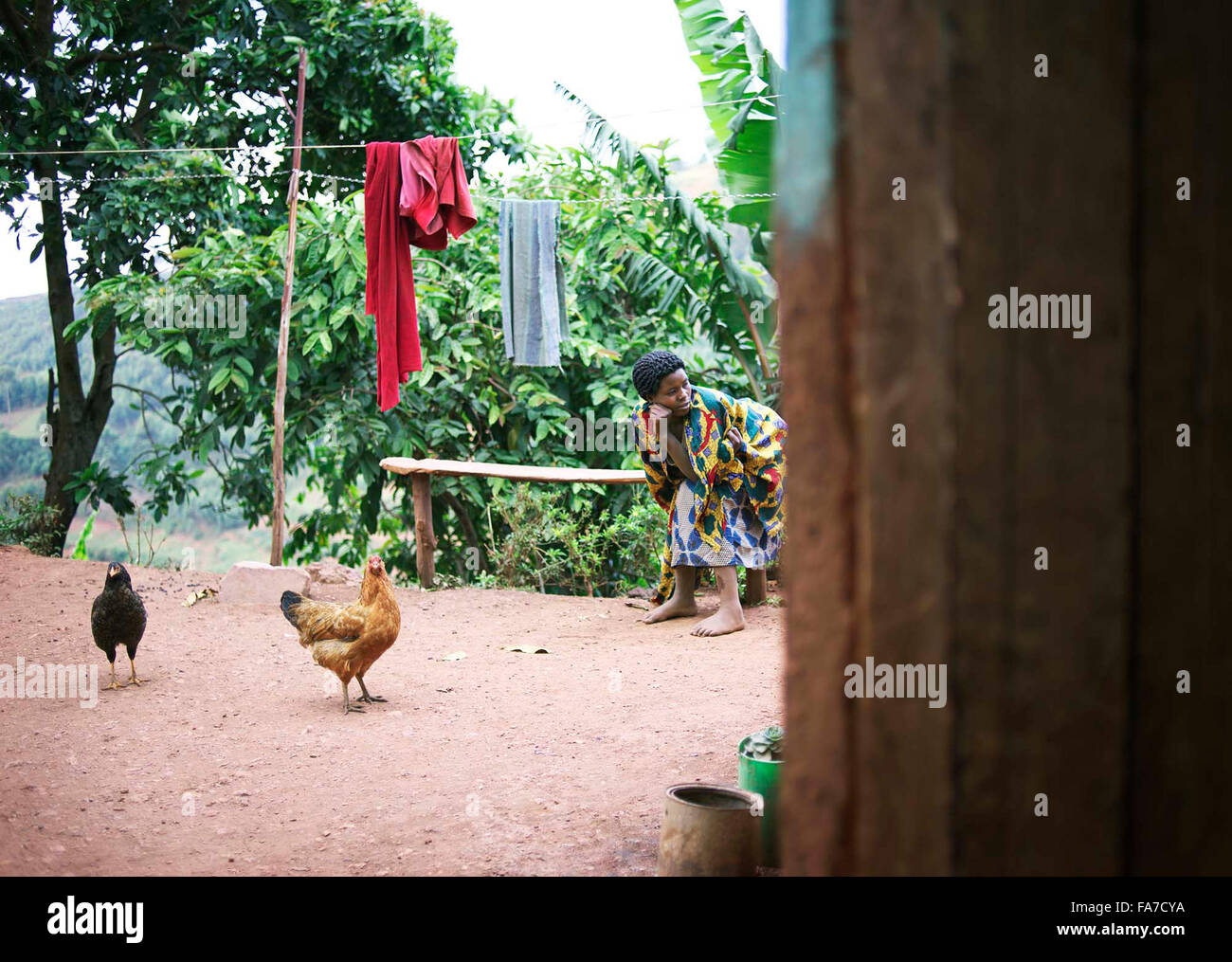 Femme ougandaise assis sur banc en bois en milieu rural avec des poules et d'animaux de cour Banque D'Images