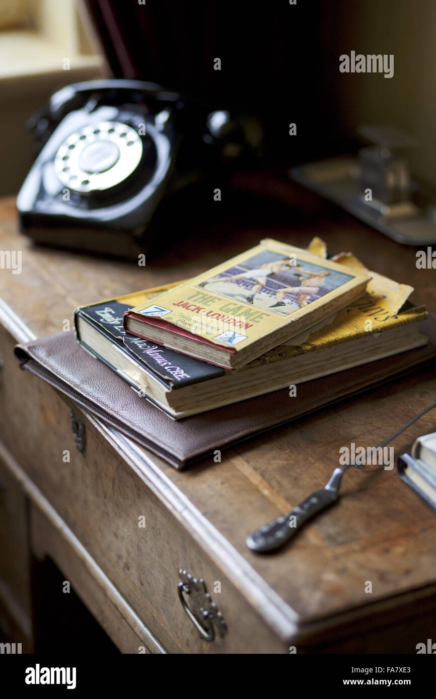 Détail d'un bureau avec des livres, un ouvre-lettre et téléphone, dans le salon/bureau, lieu Nuffield, Oxfordshire. La maison a été conçue et construite en 1914 et a été la maison de William Morris, Lord Nuffield (1877-1963), constructeur du moteur, à partir de 1933 unti Banque D'Images