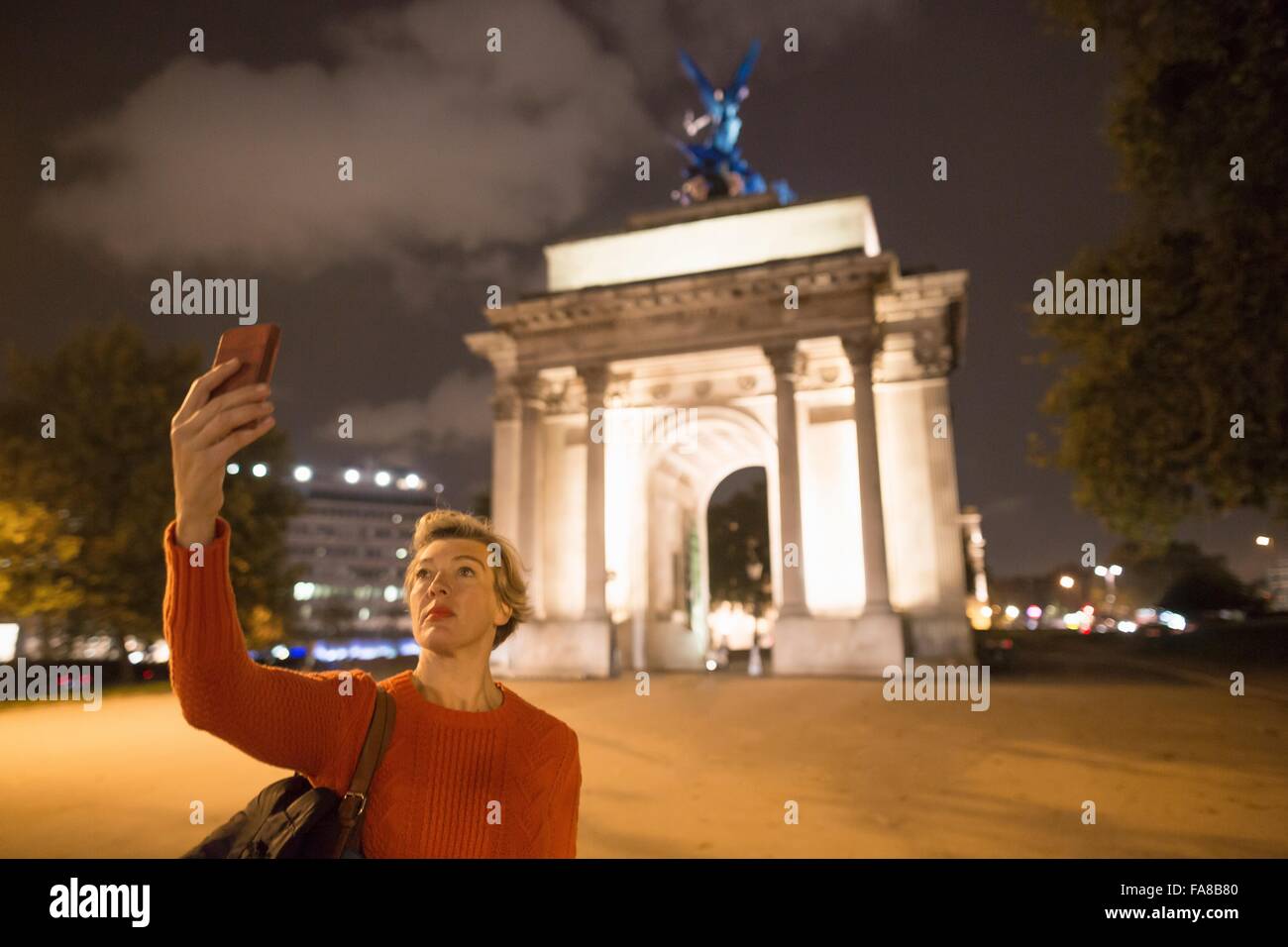 Femelle adulte prenant touristiques selfies smartphone de Wellington Arch at night, London, UK Banque D'Images