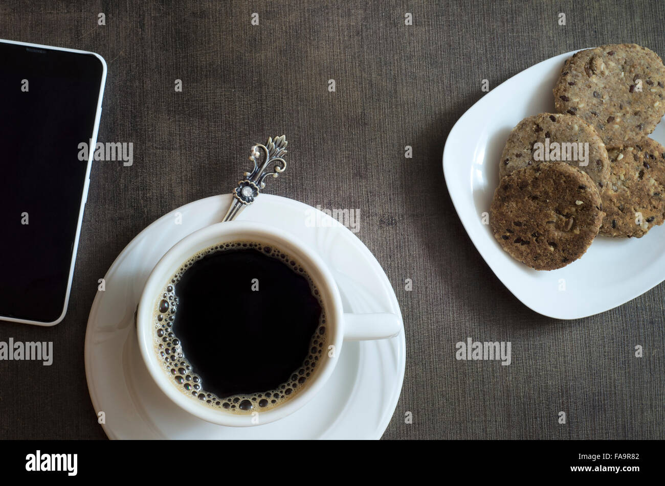 Tourné directement au-dessus de la tasse de café, les cookies d'un téléphone sur la table en bois Banque D'Images