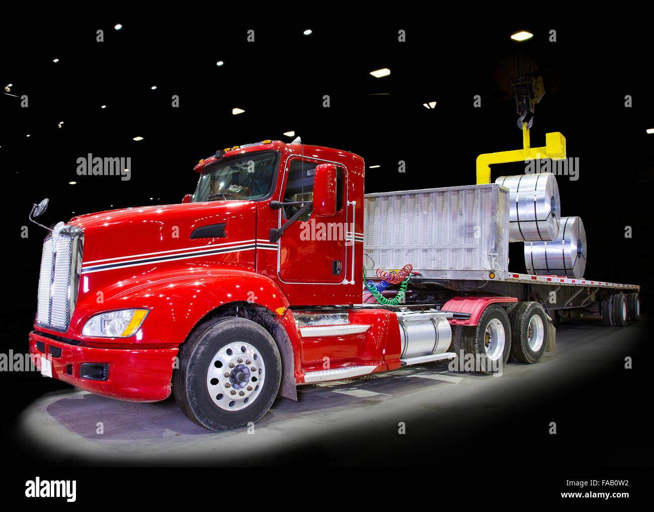 Semi remorque tracteur rouge en cours de chargement de camion avec des bobines d'acier formé à rouleau - black bay sous plafond lumineux Banque D'Images