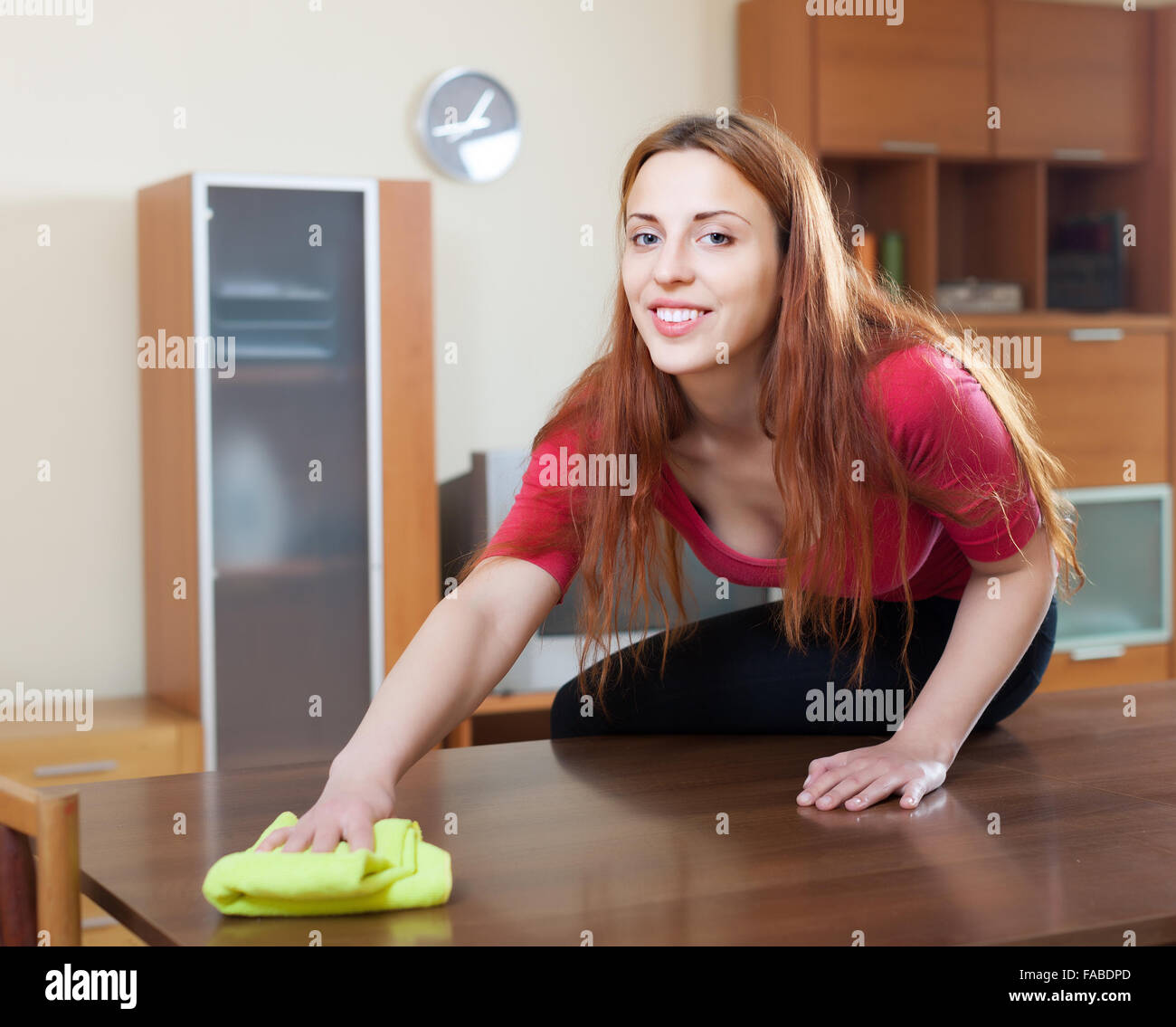 Cheerful long-haired woman in red table en bois avec nettoyage rag a home Banque D'Images