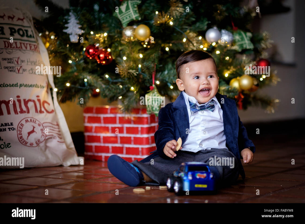 Cute hispanic bébé enfant, formellement habillé, bénéficiant de Noël journée avec nouveau jouet voiture. Banque D'Images