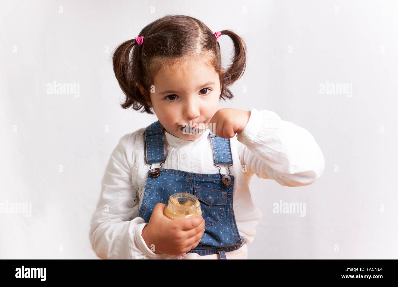 Portrait of happy girl eating fruit un pot de nourriture pour bébé. Plus isolé sur fond blanc Banque D'Images